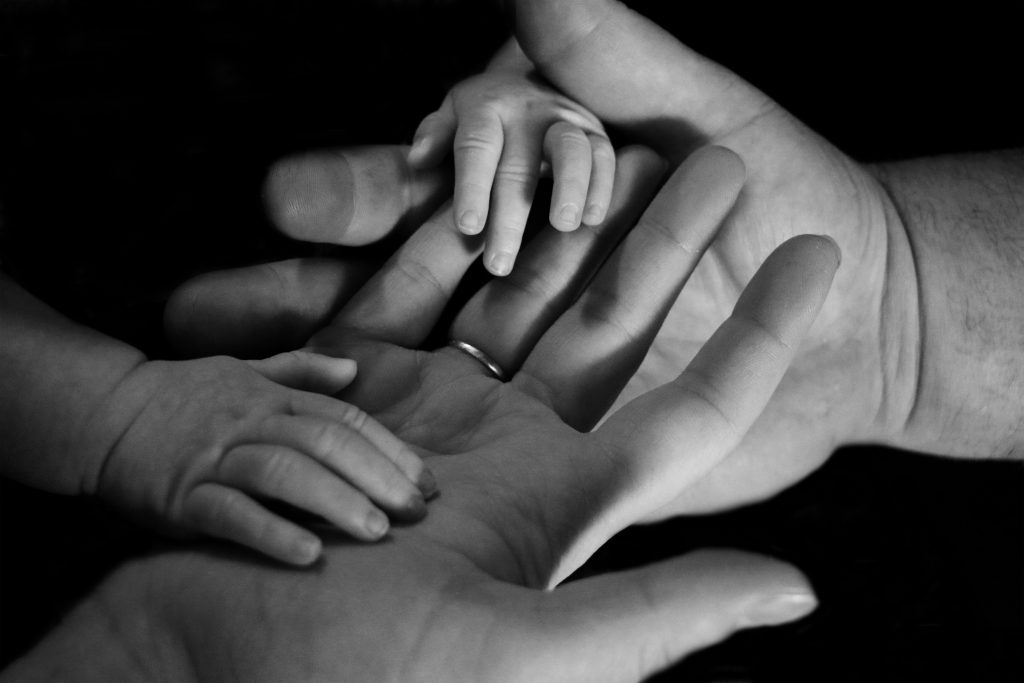Eltern halten Babyhand – Symbol für Geborgenheit
